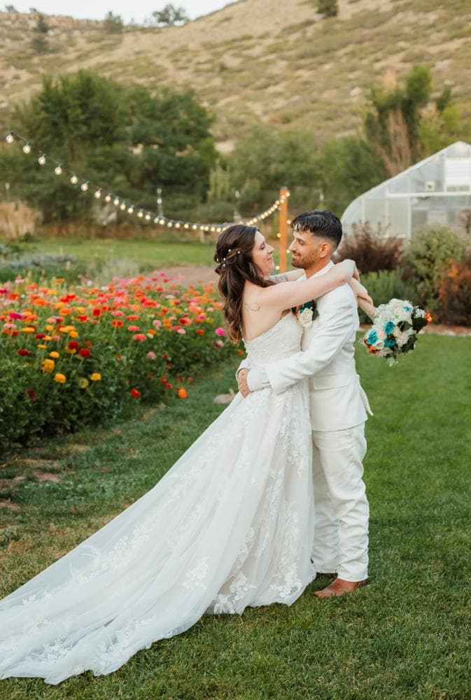 Bride and groom embracing beside a vibrant flower garden surrounded by lush greenery, Colorado wedding