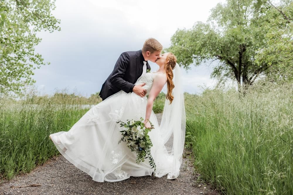 Bride and groom dip kiss surrounded by tall green grass, Northern Colorado wedding