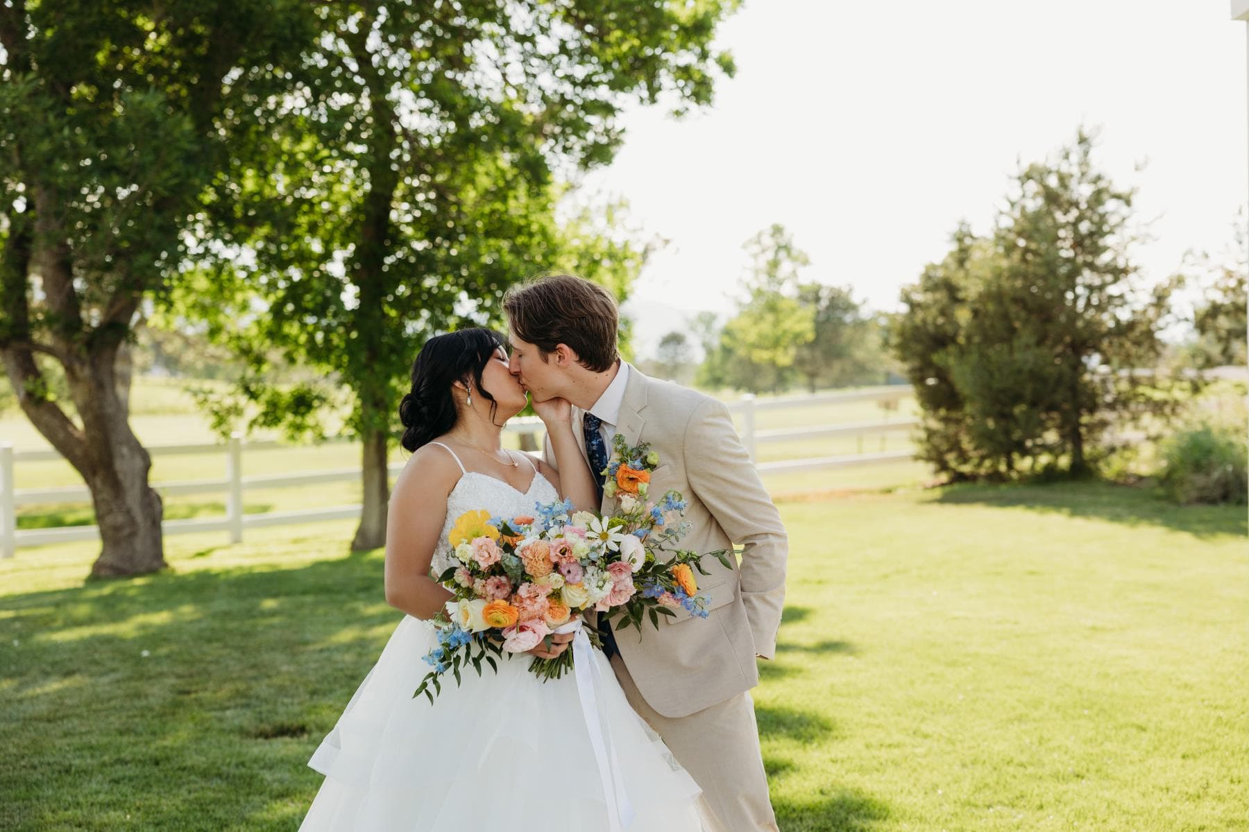 Bride and groom kissing among lush greenery with a bright bouquet, Colorado wedding
